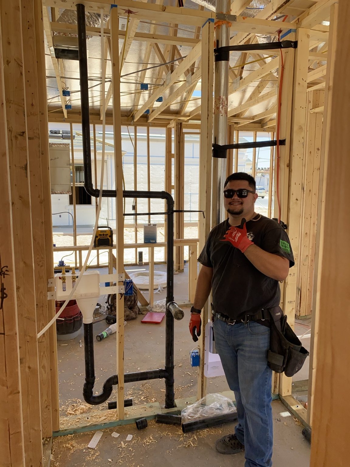 Danny standing in front of new construction rough-in plumbing and framing